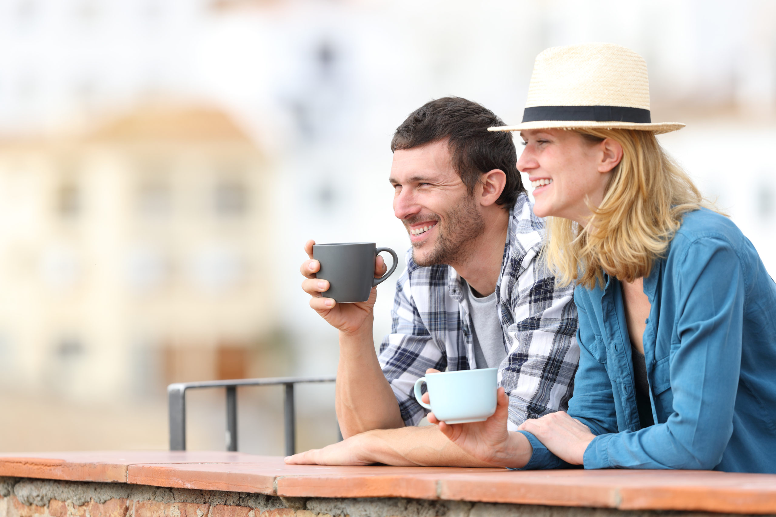 Couple of tourists drinking coffee and looking away in a balcony