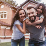 Family smiling in front of house