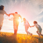 Family holding hands in field at sunset