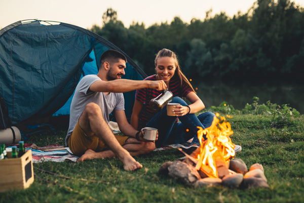 A couple outside a tent in front of a fire pouring coffee