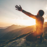man on mountain at sunset reaching toward heavens