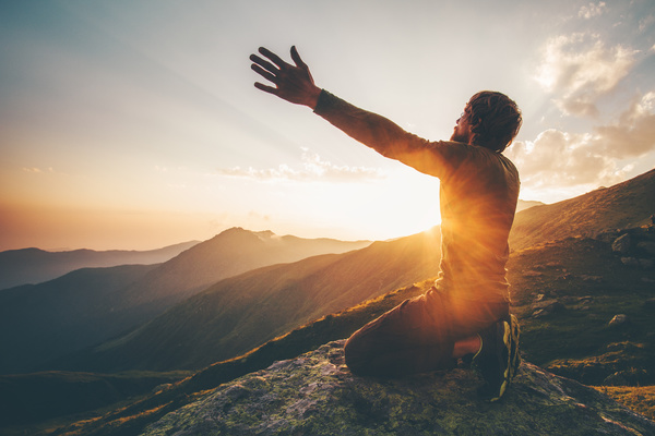 man on mountain at sunset reaching toward heavens