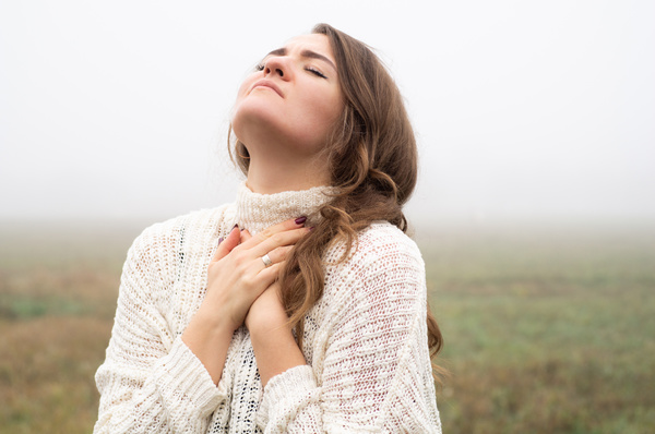 Woman with eyes closed looking up to sky in foggy field